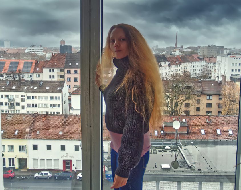 Junge schlanke Frau steht vor großem Fenster. Schönen Ausblick über die Dächer der Stadt. Dunkle Wolken