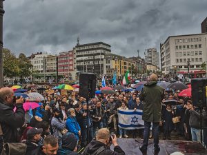 Kundgebung. Im Vordergrund Redner. Dahinter Israelfahne